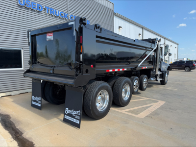 2023 Mack GR64F dump truck rear and side view showing black dump box, triple rear axles, and rear mudflaps with branding.