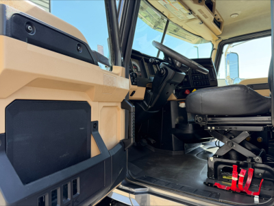 Cab interior of 2023 Mack GR64F dump truck showing steering wheel, dashboard, and driver's seat with red foot pedals and beige exterior panels.