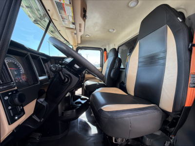Truck cab interior showing steering wheel, driver seat and passenger seat with beige and black upholstery; dashboard with gauges and center console visible.