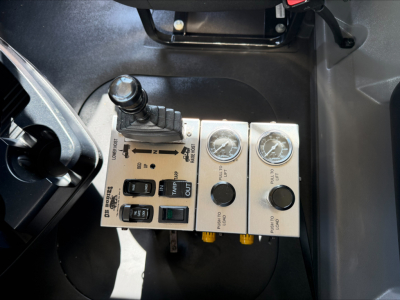 Dump truck cab control panel with levers, gauges and switches, including labels for toggles and gauges.