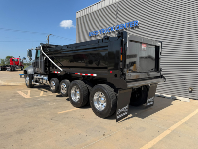Dump truck in a dealership lot showing a black Mack GR64F dump bed with three rear axles and chrome wheels.
