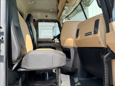 Mack GR64F dump truck interior cabin view showing driver seat, steering wheel, and dashboard with beige panels.