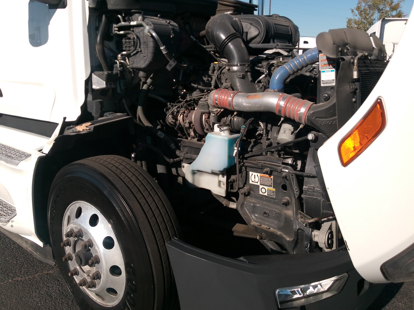 Peterbilt 579 engine bay with visible turbocharger, hoses, and radiator; side view of front wheels and fender; intake piping and coolant reservoir.