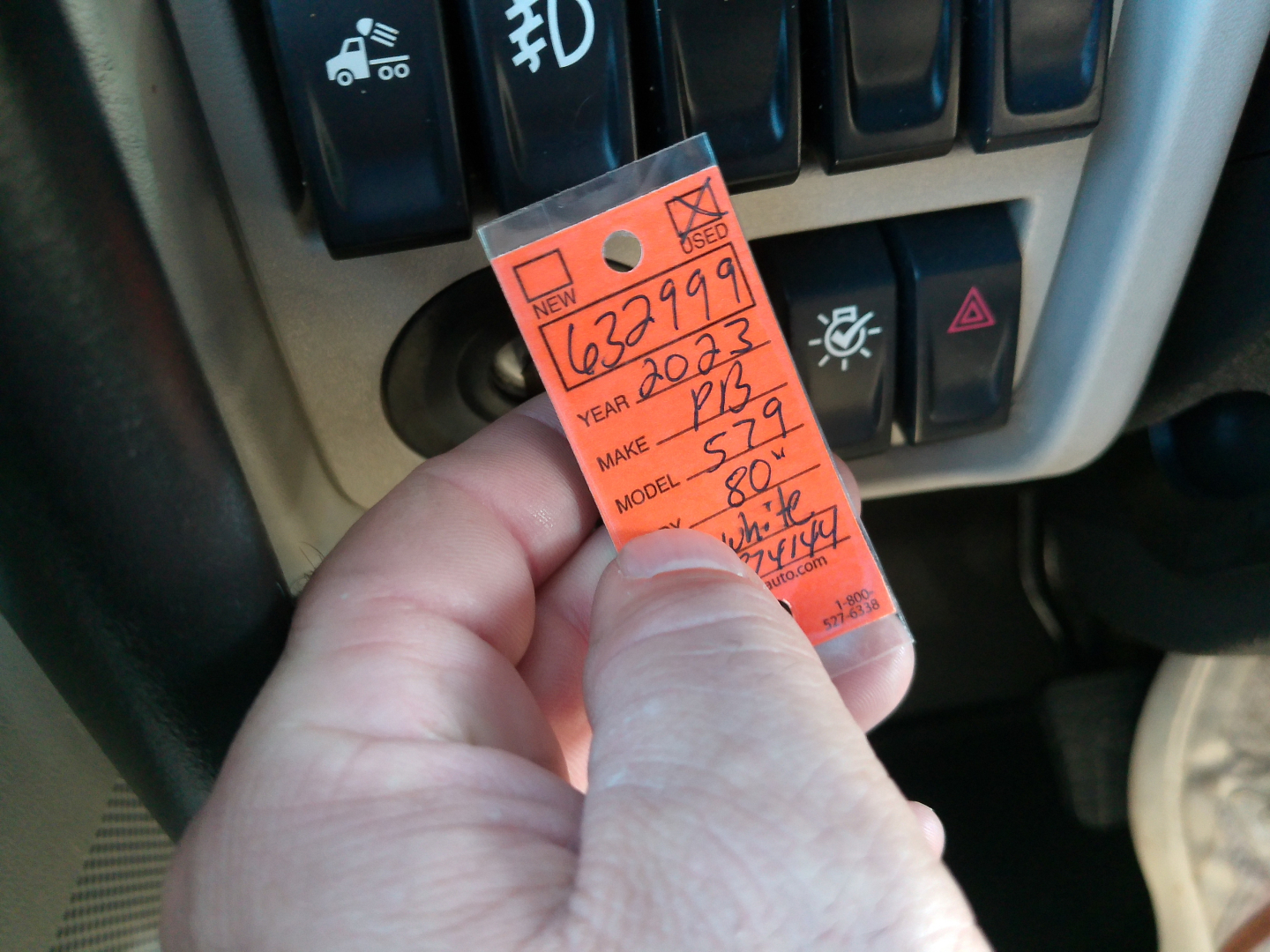 Vehicle tag with VIN 1XPBDP9X9PD874144 held near dashboard switches in a Peterbilt 579 interior.