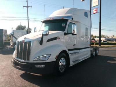 Peterbilt 579 conventional sleeper tractor in white, front three-quarter view, chrome grille, dual mirrors, daytime running lights.