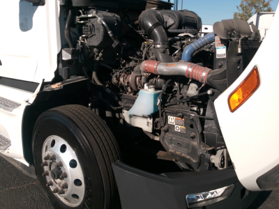 Peterbilt 579 engine bay with visible turbocharger, hoses, and radiator; side view of front wheels and fender; intake piping and coolant reservoir.