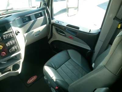 Peterbilt 579 truck interior view showing driver seat, dashboard, steering wheel, and door panel with window controls and Peterbilt logo.
