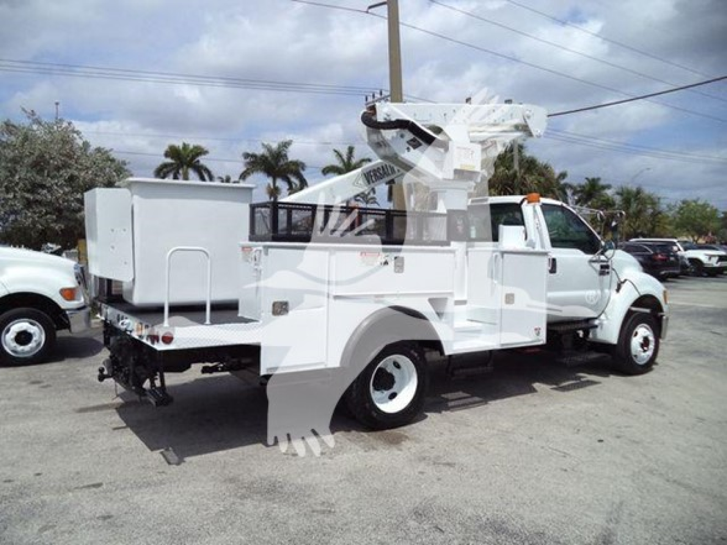 Versalift VST40i crane truck in-service with elevated boom folded over cab, white utility body, rear outriggers, and mounted crane equipment.