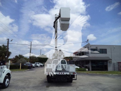 Versalift VST40i aerial work platform mounted on truck; boom raised; crane-type equipment visible with white and gray color; background includes dealership building and parked vehicles.
