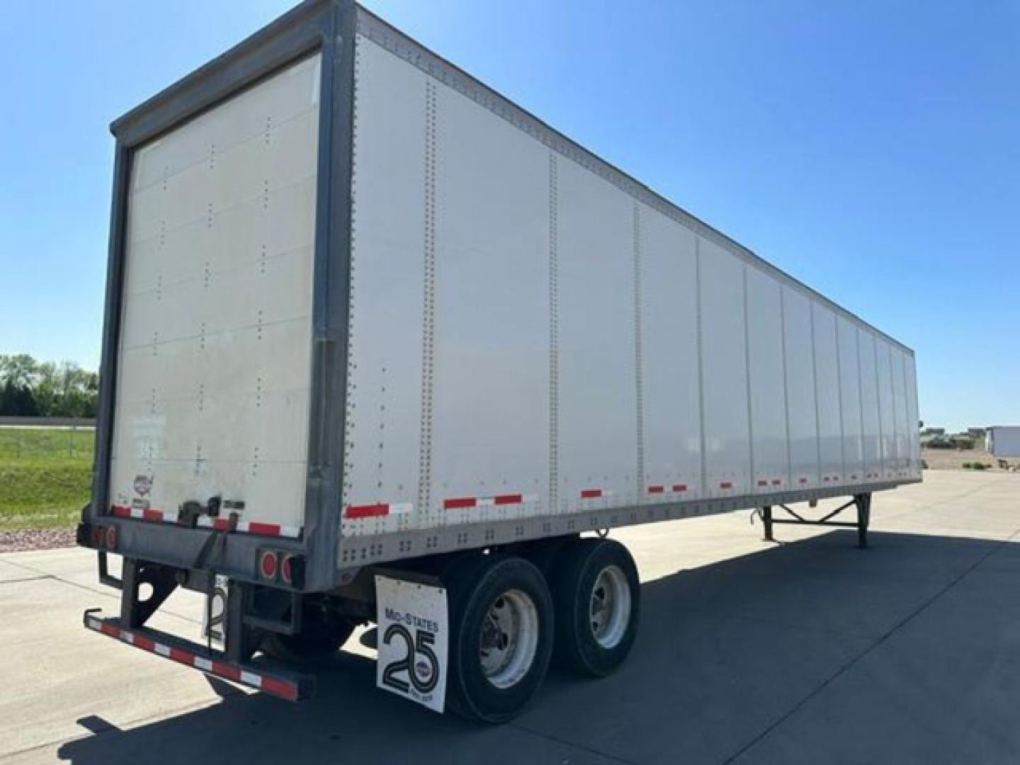 Trailer side view showing a 2016 Wabash box trailer with dual rear axles and gray riveted panels.