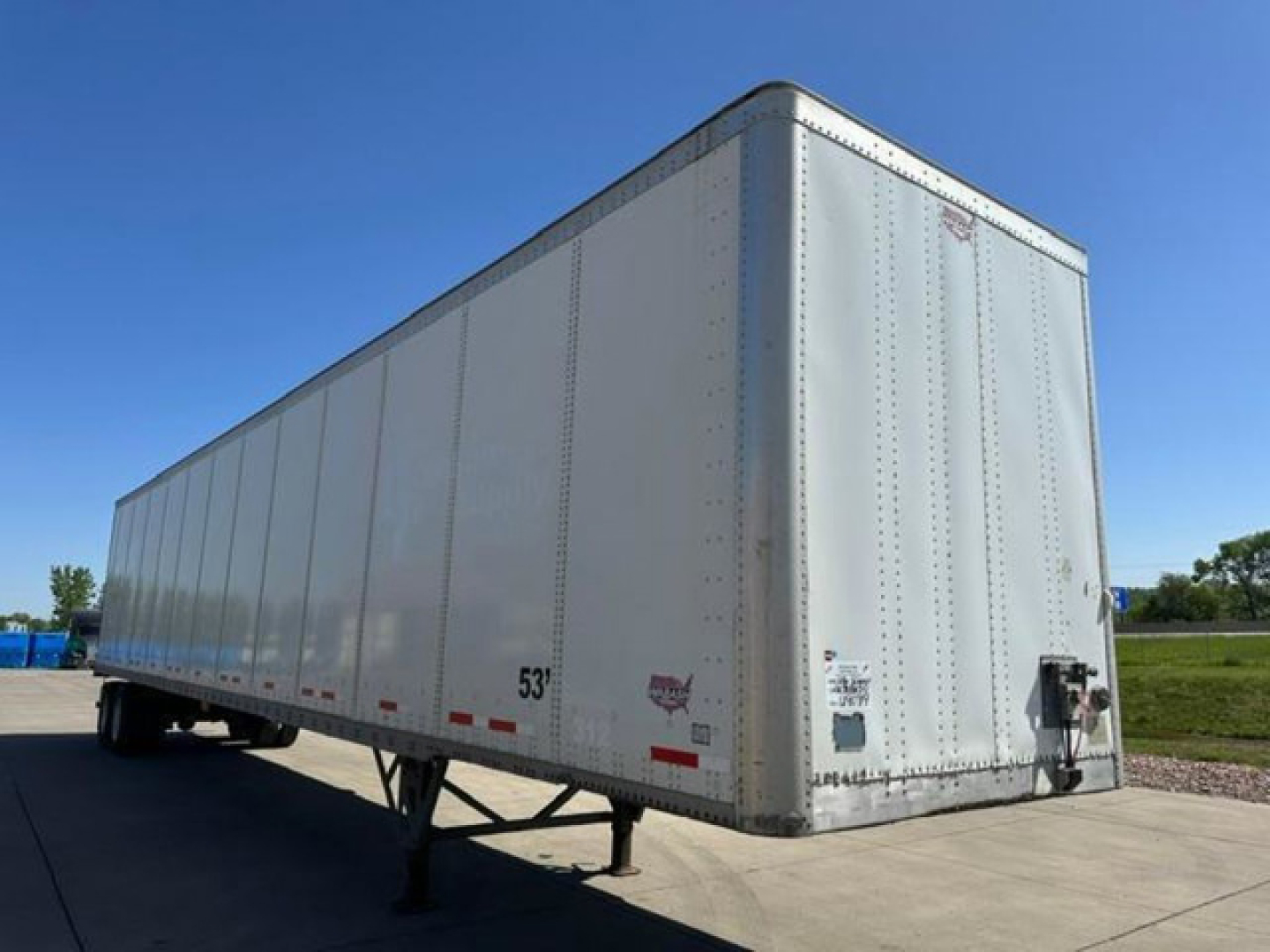 Trailer side and front of a white 53' Wabash van trailer showing no branding text legibly visible. Visible numbers: 53' length marking on side near rear. Front corner shows hitch and rear equipment.