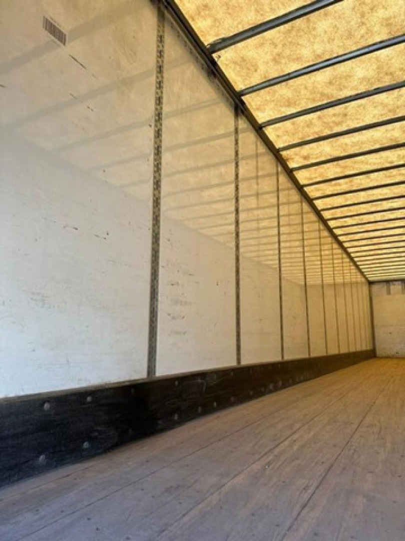 Trailer interior showing wooden floor and white sidewalls with ribbed metal framing, long empty cargo trailer.