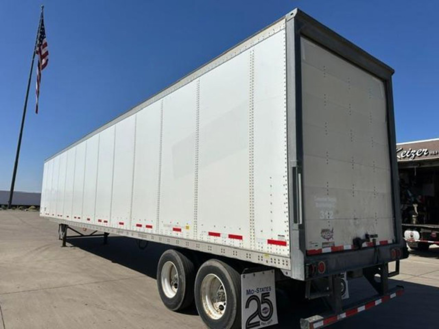 Trailer showing side and rear of a white 2016 Wabash van trailer with dual rear axles and a roll-up door. VIN 1JJV532D7GL908650 visible in listing.