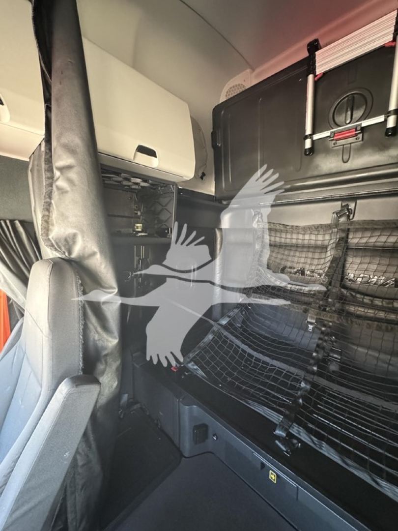 Cab interior of a Freightliner Cascadia cabin showing sleeper area with panels, storage cabinet, and mesh side netting.