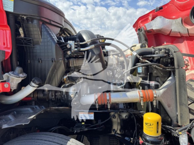 Truck engine bay of a 2023 Freightliner Cascadia showing component labels, hoses, and a yellow SENTRY DEF reservoir cap.