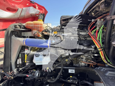 Engine bay of a Freightliner Cascadia showing coolant reservoir, radiator, hoses, wiring, and a blue silicone hose cover.