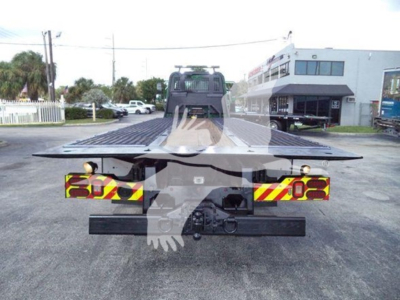 Flatbed rollback truck rear view showing reflective chevrons and license/bolt area, with a chrome hitch and black bumper