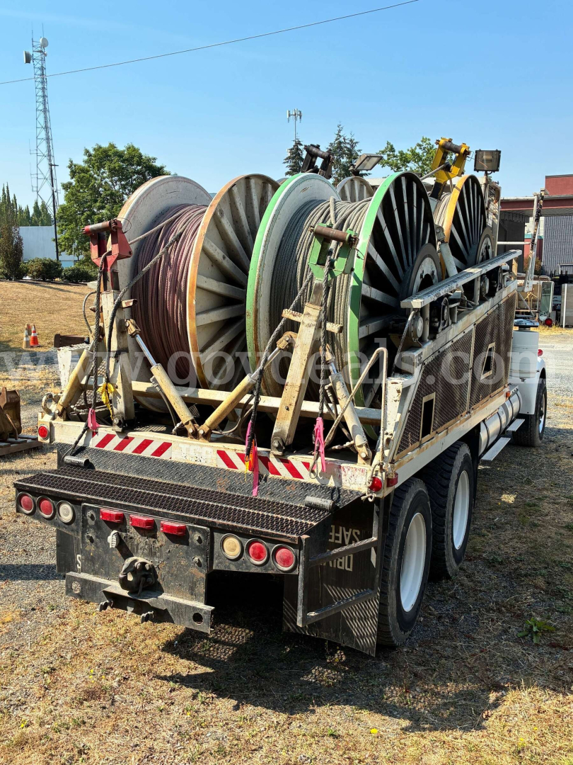 Kenworth W900A truck bed with multiple large reels of cable on a flatbed trailer, rear view, utility equipment, assorted colors on reels.