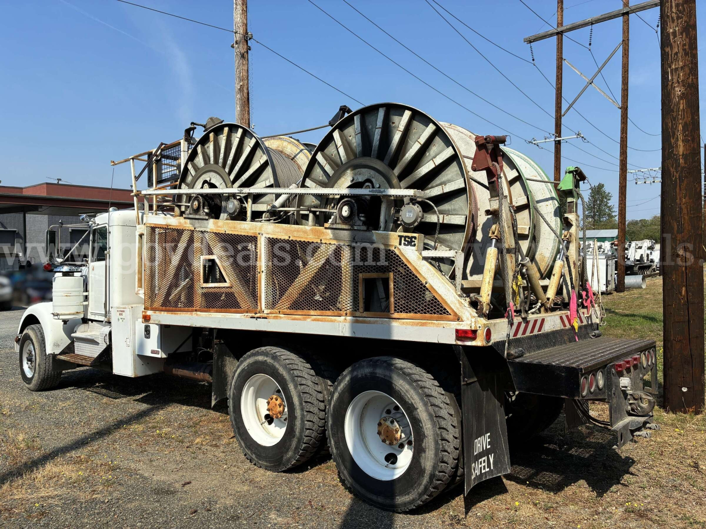 Kenworth W900A service truck with a flatbed carrying large cable reels, rear view showing dual rear axles and wheel rims.