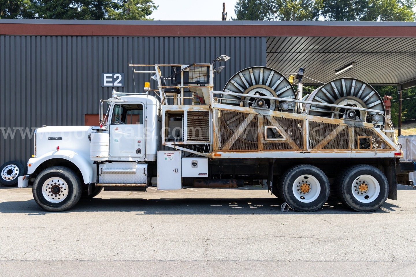 Kenworth W900A dump-style truck side view with large spool winders on flatbed and steel framework.