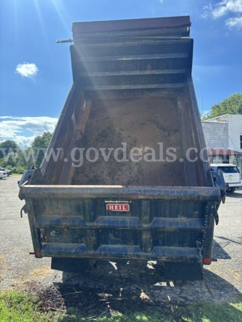 Dump truck bed raised showing interior with rust and dirt, rear view of blue Ford F-750 dump truck with HEIL tag on tailgate.