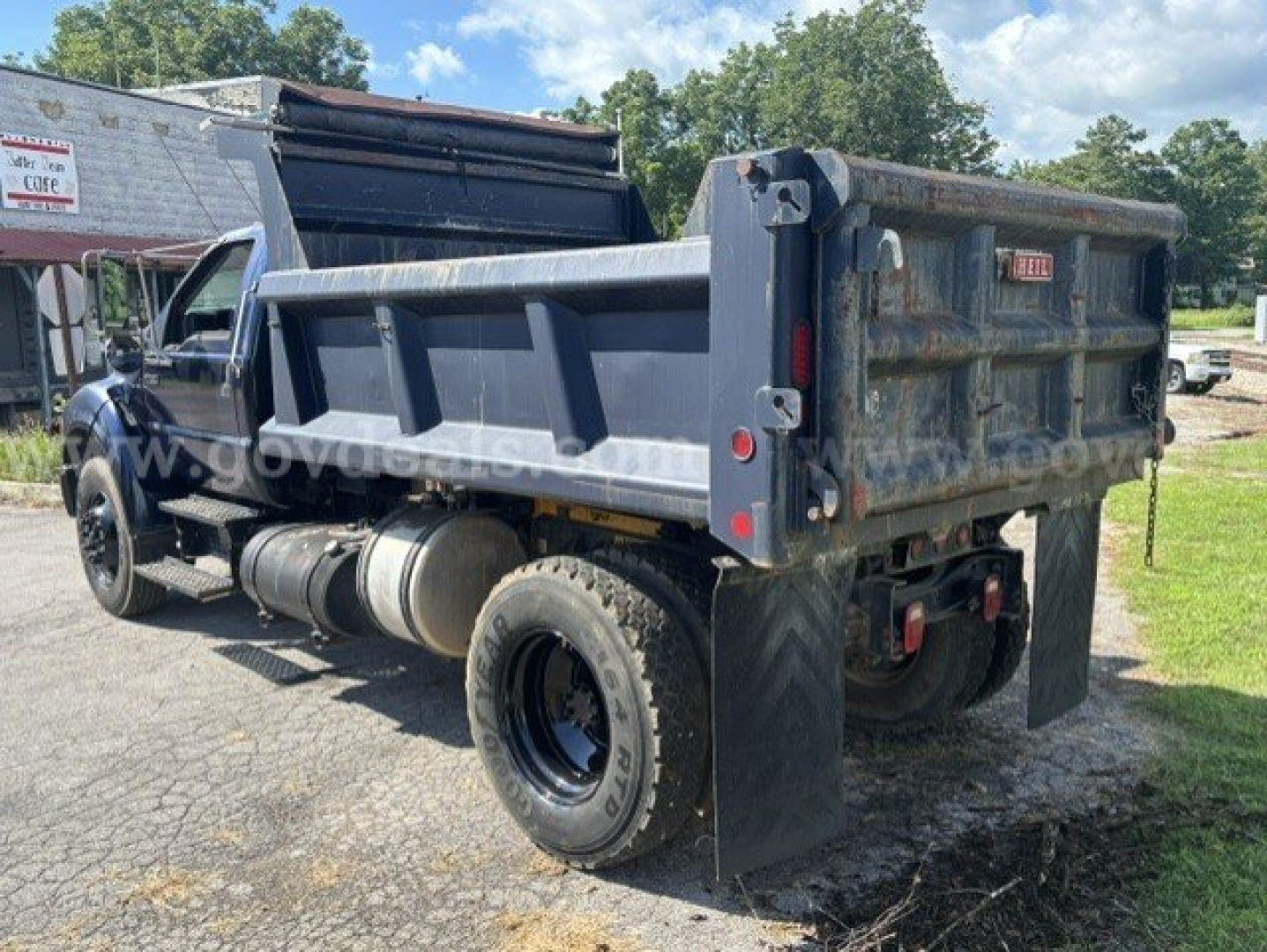 Dump truck bed and rear view of a 2006 Ford F-750 dump truck with a gray bed, dual rear tires, and hydraulic tailgate; visible wear and dirt on body panels.