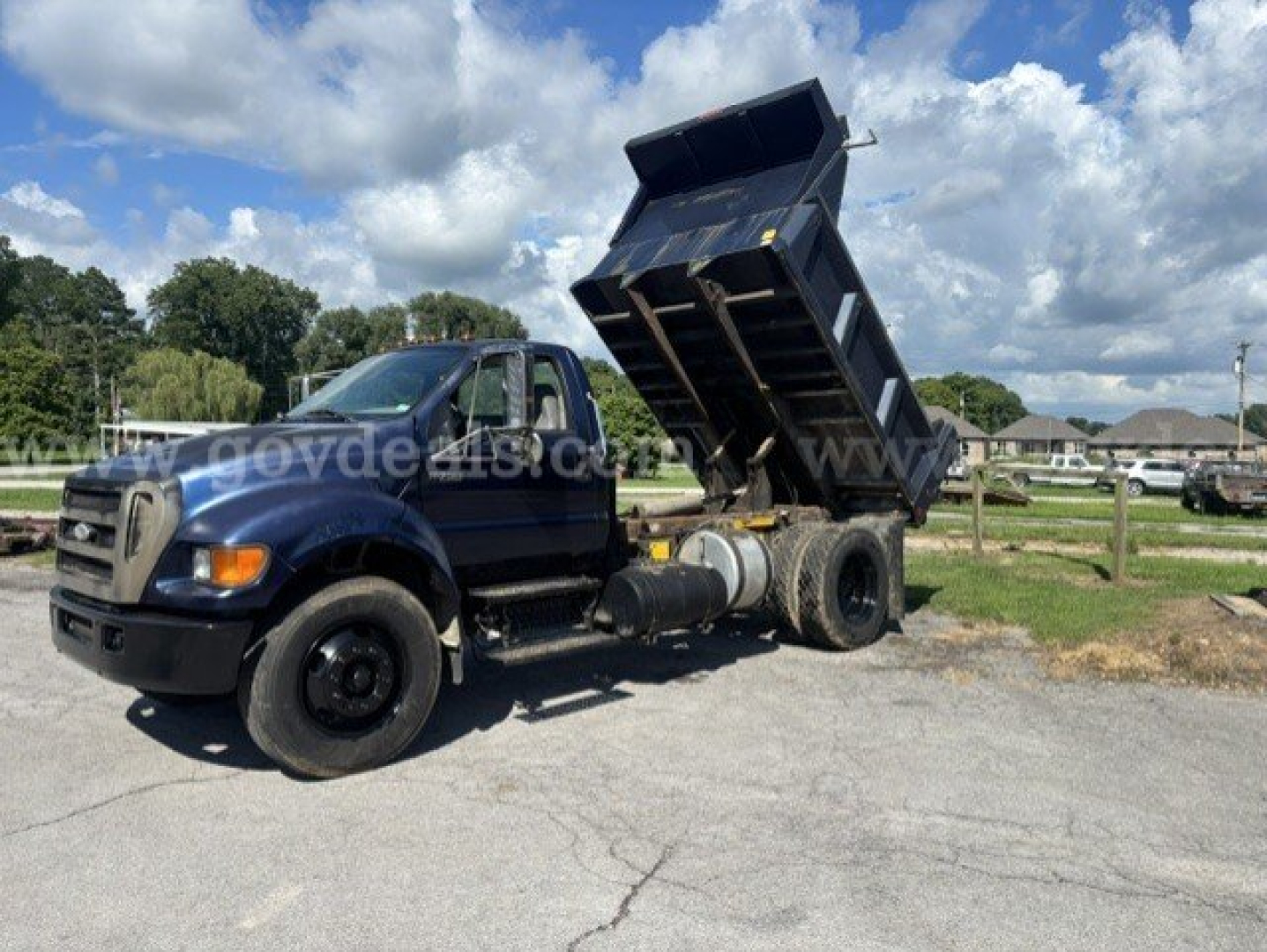 Ford F-750 dump truck with hydraulic bed raised, side view showing cab and dual rear axles.