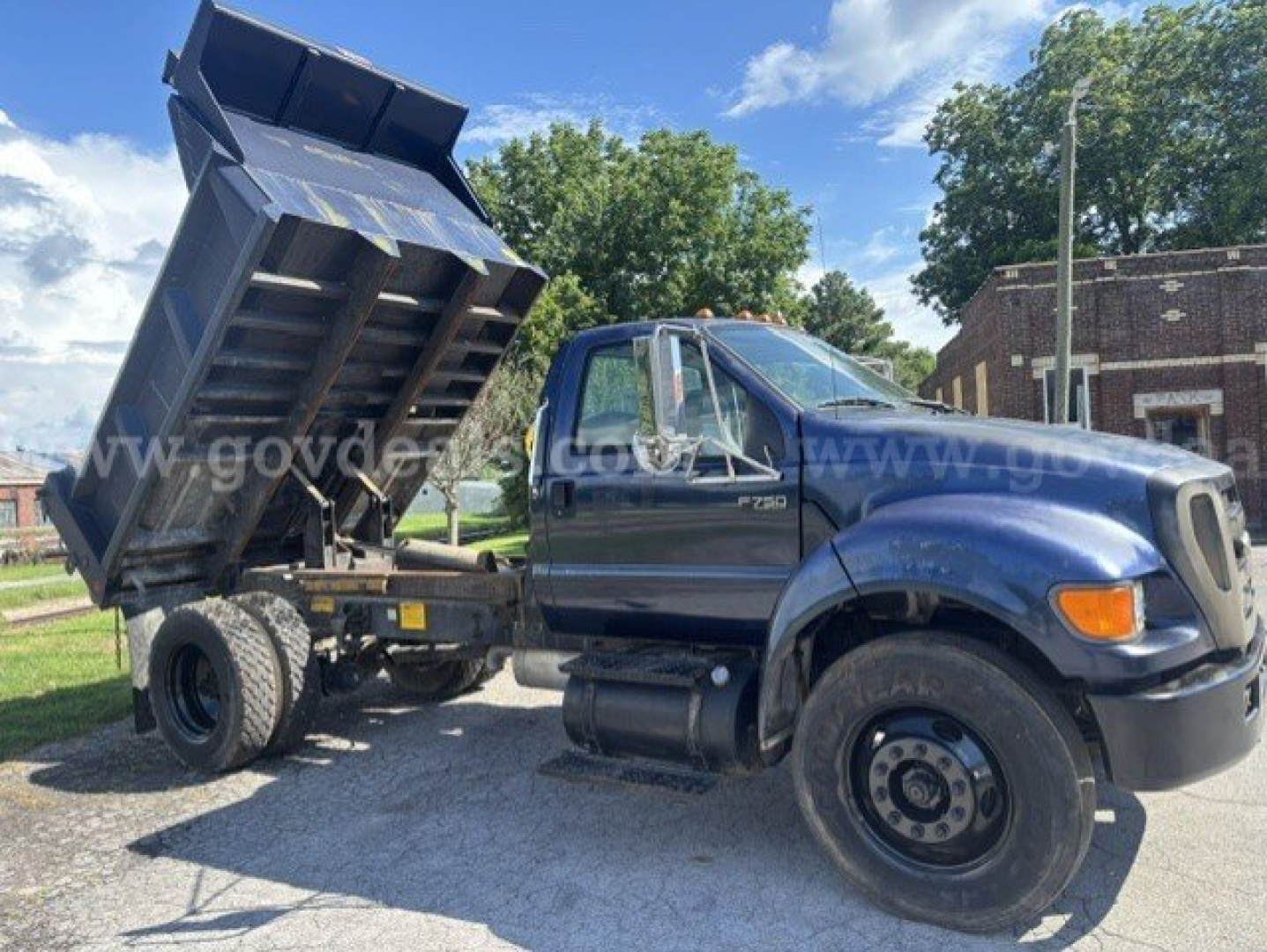 Ford F-750 dump truck with bed raised, blue cab, side view showing F-750 badge and dump bed in elevated position.