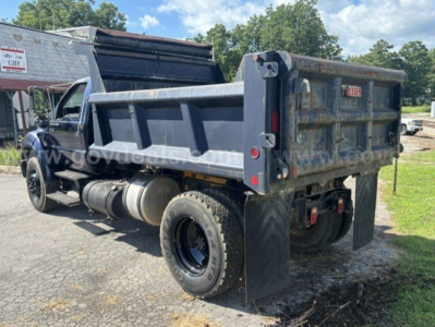 Dump truck bed and rear view of a 2006 Ford F-750 dump truck with a gray bed, dual rear tires, and hydraulic tailgate; visible wear and dirt on body panels.