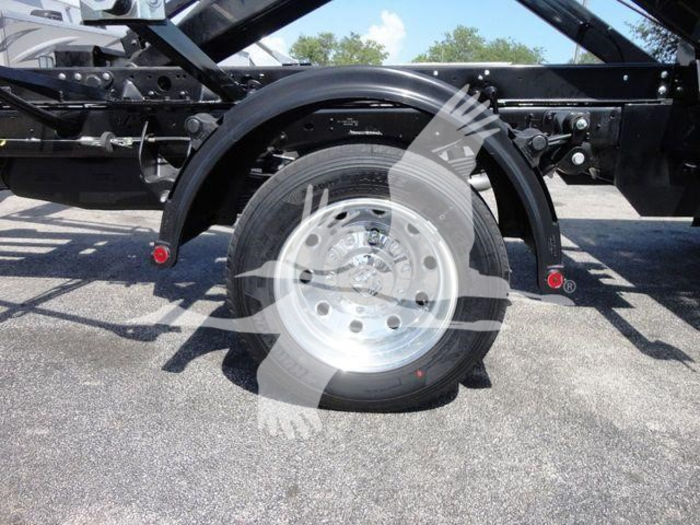 Truck wheel and suspension view showing single rear axle, heavy-duty frame, and aluminum lugged wheel on a Ram 5500 roll-off truck.