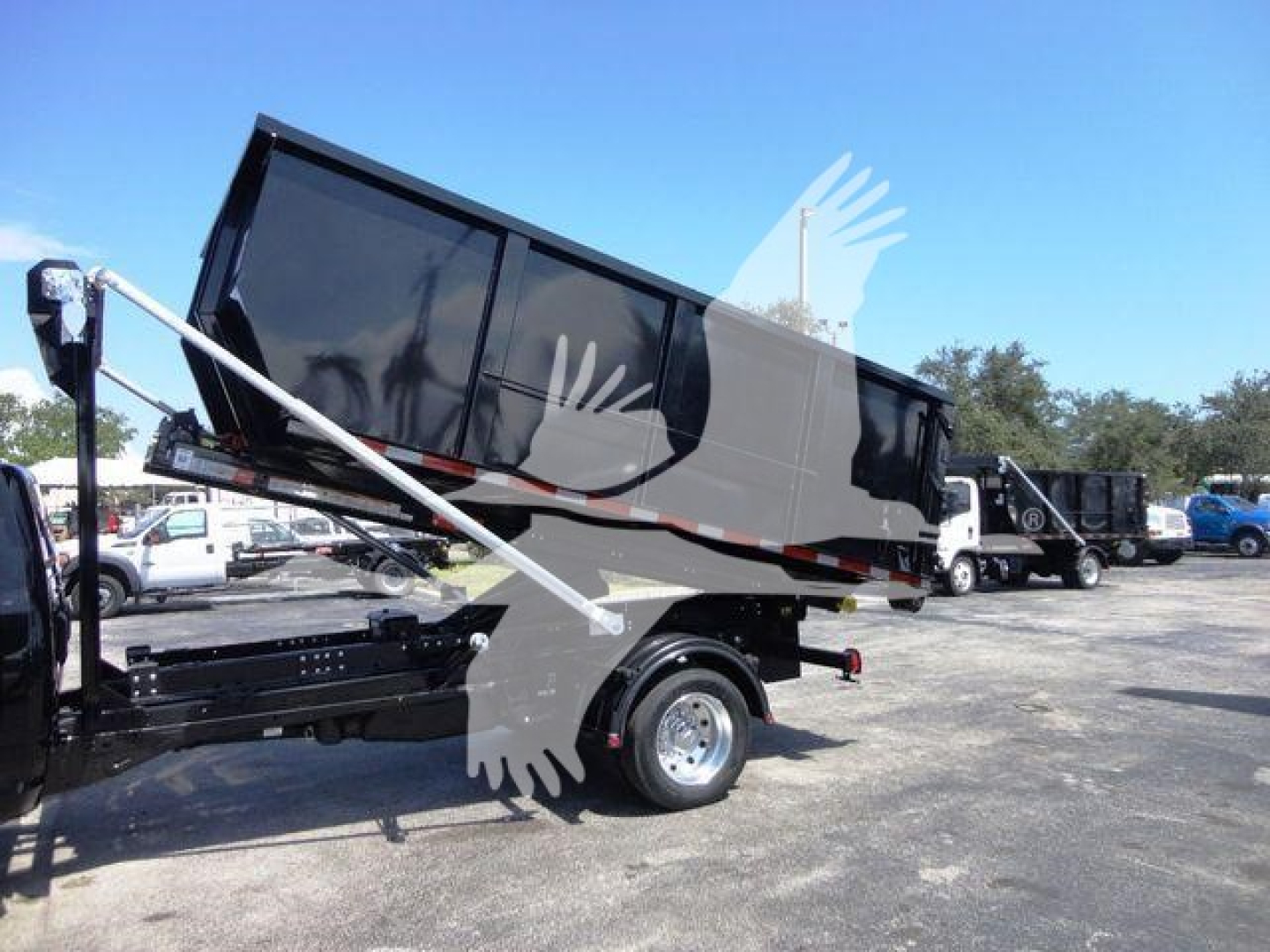Ram 5500 dump truck bed elevated on a rollout hoist in a dealership lot, with other trucks in background.