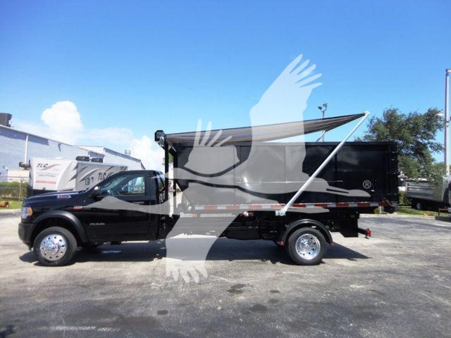 Ram 5500 dual rear wheel truck with a roll-off dump body, black color, side view showing cargo bed and tarp cover.