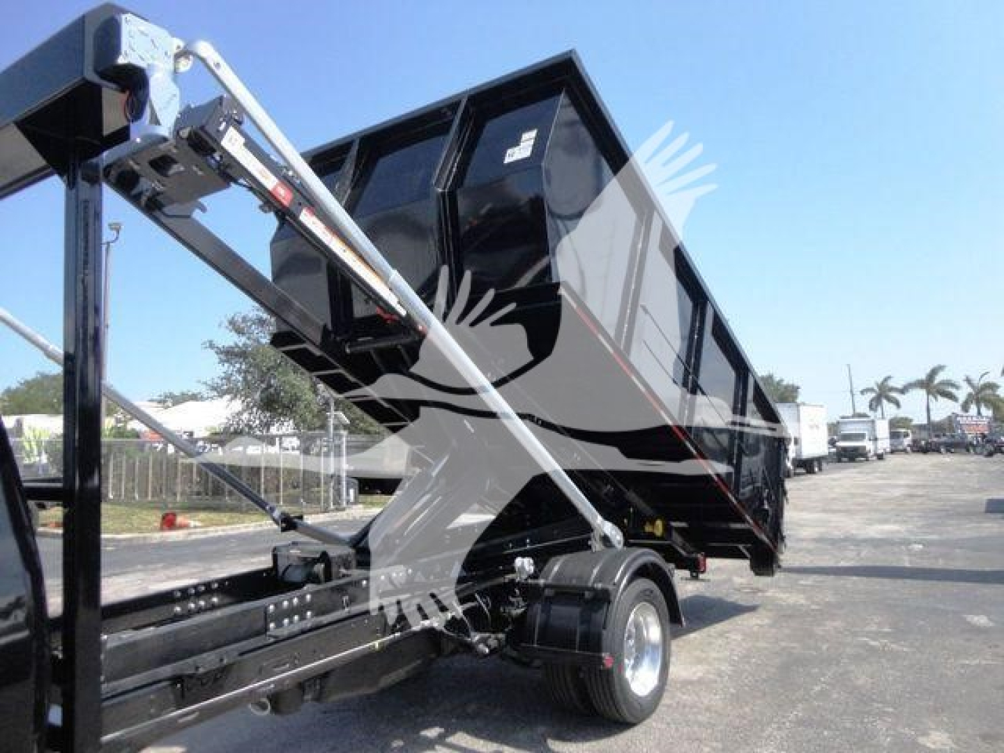 Ram 5500 rolloff truck bed with hydraulic arms and black dump body, side view showing chassis and wheel, no visible text.