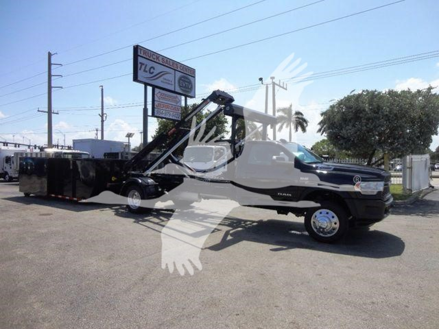 Ram 5500 HD rollback tow truck with crane arm and flatbed, side view in a dealership lot.