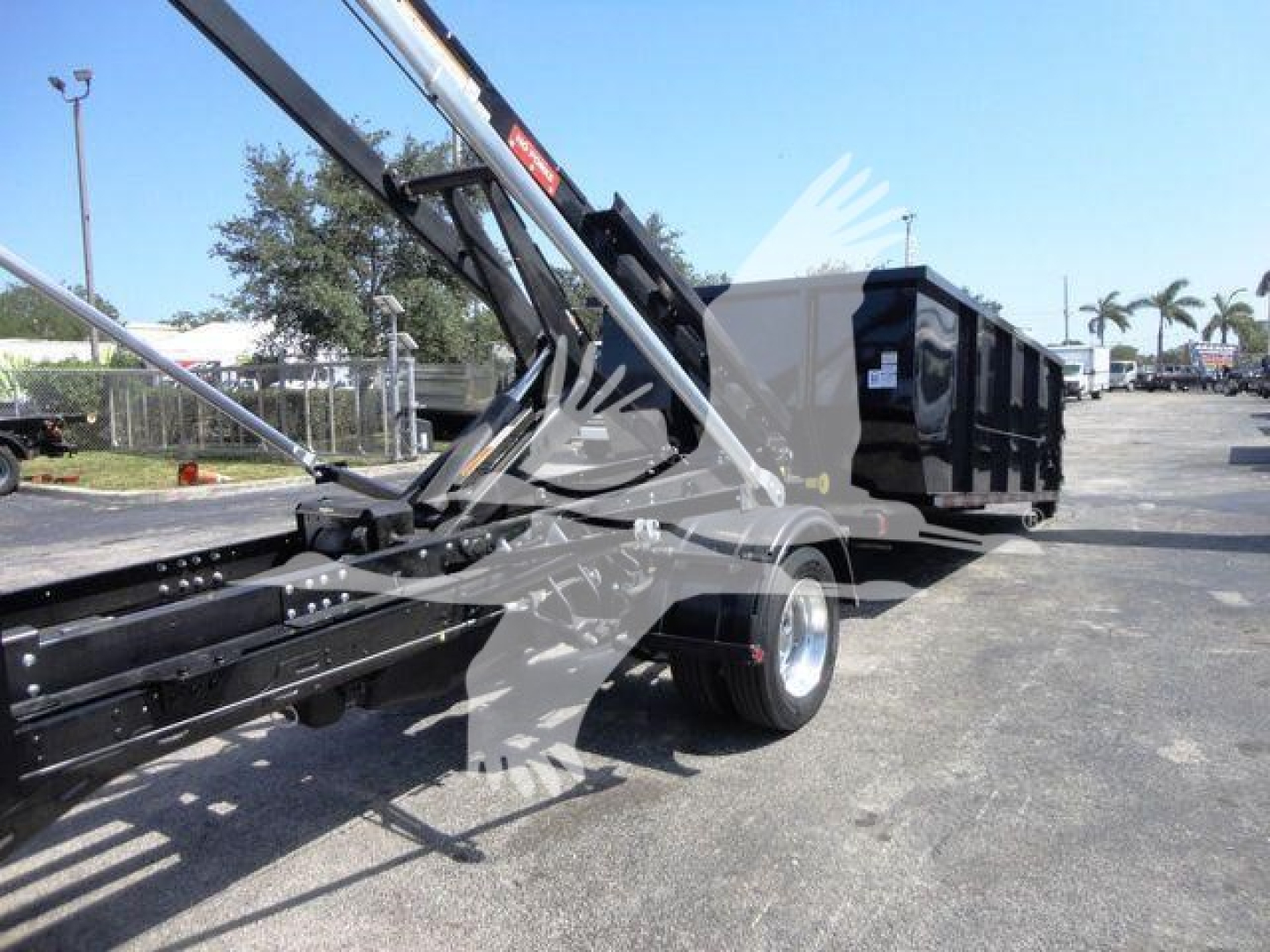 Truck bed area with a black roll-off container on a Ram 5500 chassis, hydraulic arm extending over the container, with no visible manufacturer text legible.