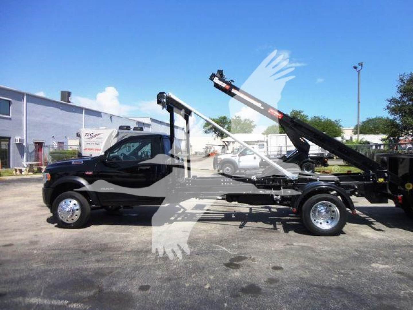 Ram 5500 tow truck/rolloff body side view showing crane arm and black cab with chrome wheels.