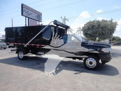 Ram 5500 dump truck with black dump body and white cab, side view, in a dealership lot.