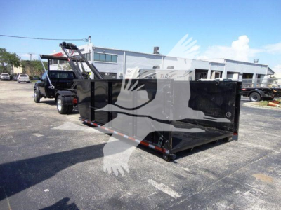 Ram 5500 dump truck in a lot with a large black roll-off dumpster attached, side view showing cargo bed and hoist mechanism.