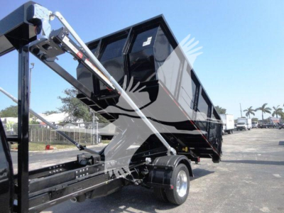 Ram 5500 rolloff truck bed with hydraulic arms and black dump body, side view showing chassis and wheel, no visible text.