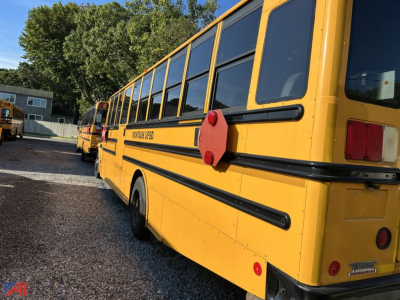 School bus side view showing yellow Freightliner bus body with black accents and rear red reflector lights.