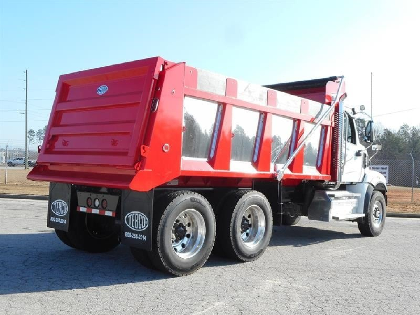 Dump truck with red dump bed and white cab, side view showing rear wheels and tailgate; no visible legible text or numbers on the truck itself.
