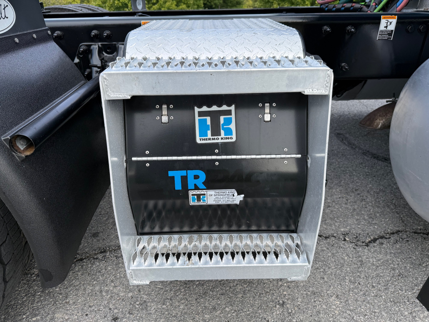 Peterbilt 579 sleeper tractor fuel/auxiliary compartment with TR logo, diamond plate box, and hydraulic lines visible.