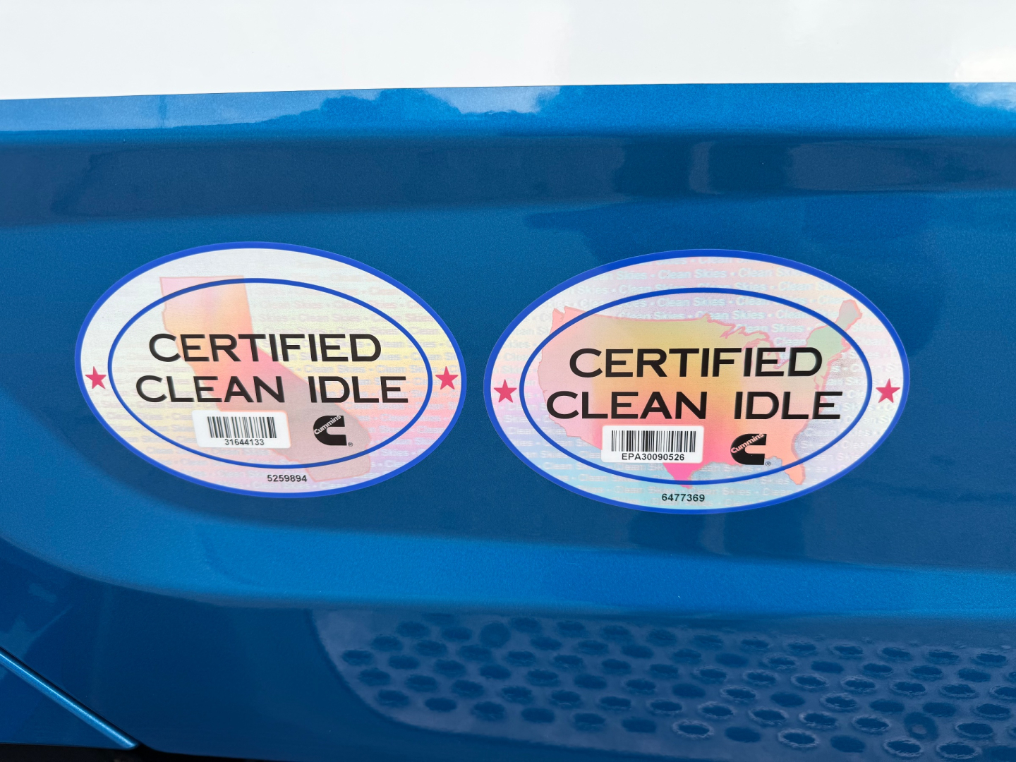 Two circular 'Certified Clean Idle' stickers on blue Peterbilt truck exterior showcasing clean-idle certification.