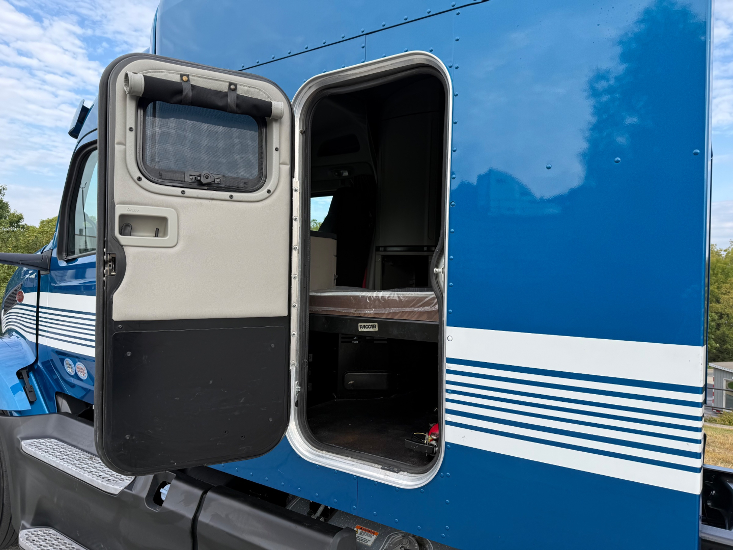 Peterbilt 579 conventional sleeper truck rear entry door open showing interior cabin step and cargo area.