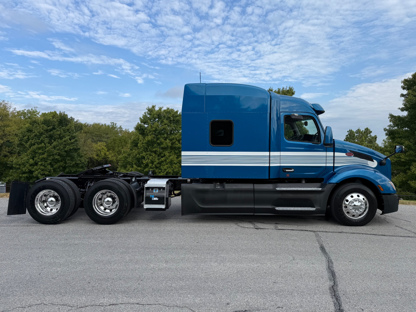 Peterbilt 579 conventional sleeper truck side view showing blue cab with white stripes and dual rear axles on a trailerless chassis.