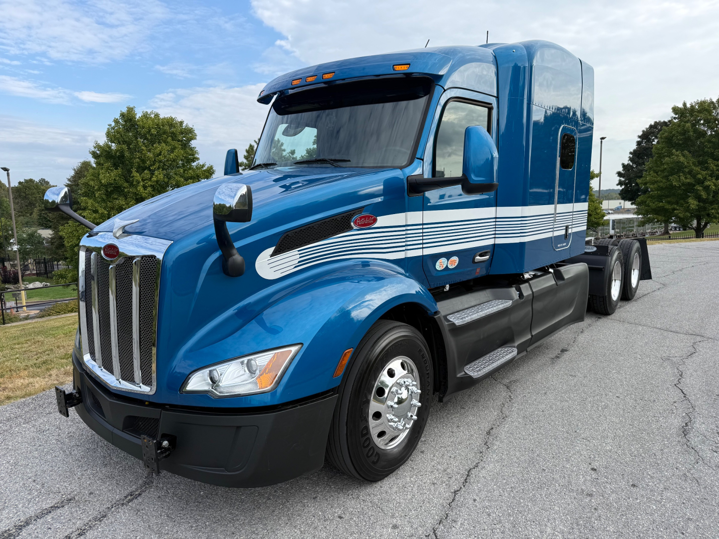 Peterbilt 579 conventional sleeper truck in blue, side view showing chrome grille, dual rear axles, and white decorative stripes.