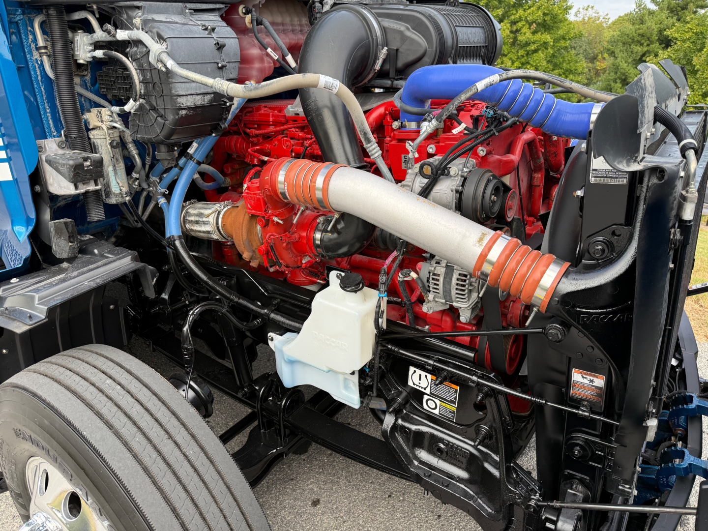 Peterbilt 579 engine bay showing red engine, blue hoses, and white coolant reservoir with surrounding components.
