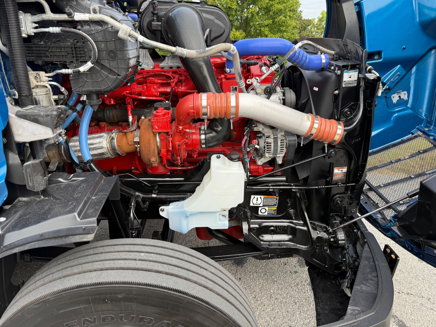 Peterbilt 579 engine bay showing red diesel engine, white coolant reservoir, blue hose, and black radiator support.