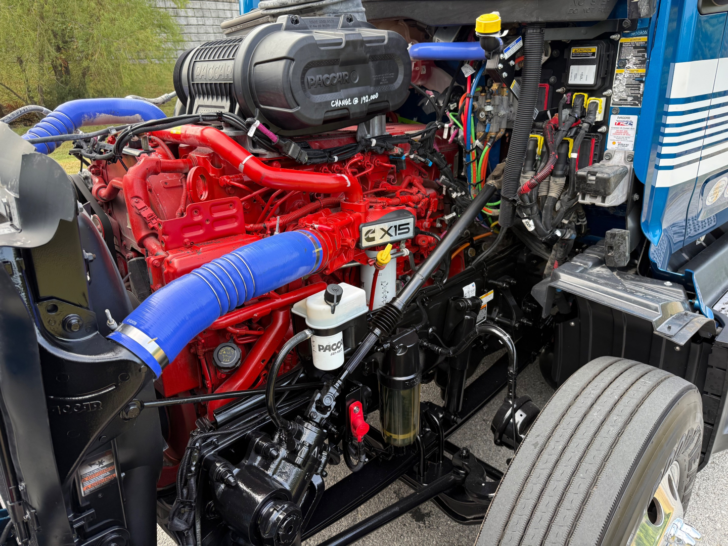 Peterbilt 579 engine bay showing red engine, blue hoses, and surrounding components.