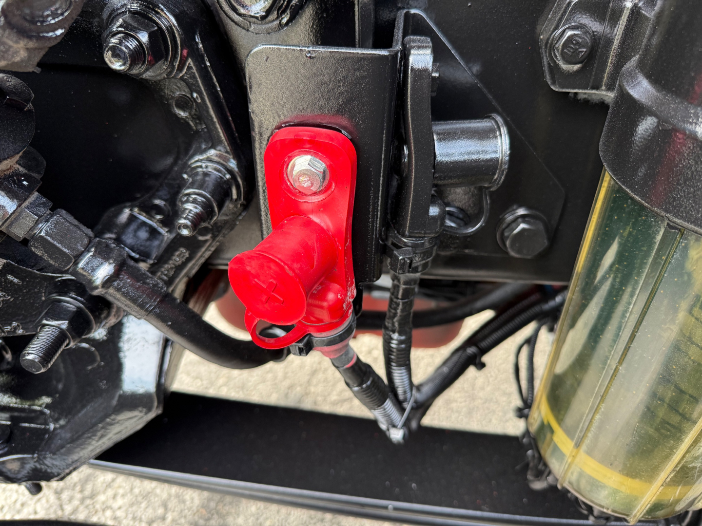 Peterbilt 579 engine bay view showing red battery disconnect switch with red cap, nearby hoses and metal brackets